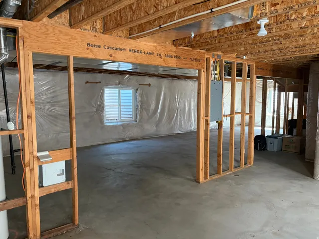 Unfinished basement space featuring exposed wooden joists and framing, concrete flooring, window with louvered blinds, and visible electrical panels
