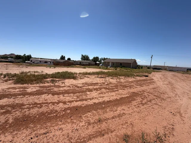 Expansive open lot featuring a clear sky overhead and a distant residential structure