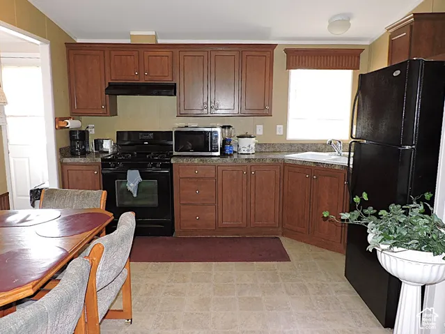 Kitchen featuring wood-finish cabinetry, black gas range, black refrigerator, and a corner sink with a window