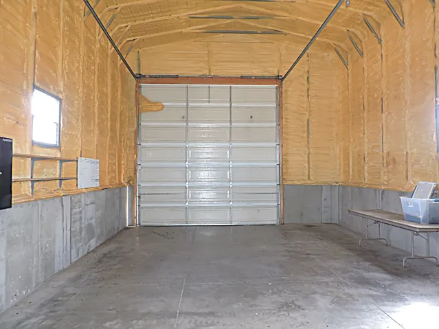 Spacious interior featuring a large roll-up door, concrete flooring, and exposed ceiling trusses