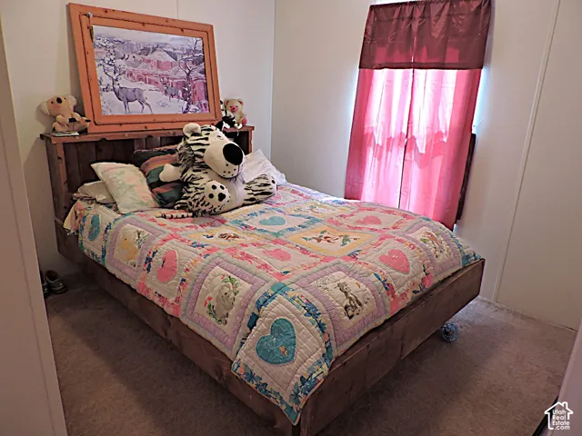 Bedroom featuring light-toned walls, a window with red privacy curtains, and carpeting