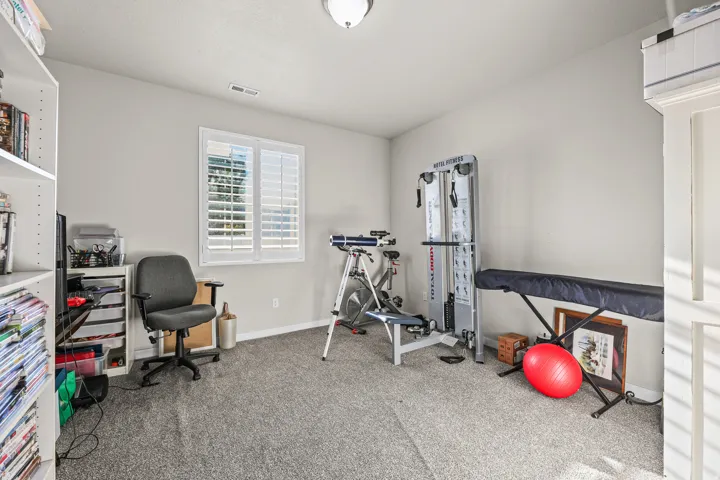 Versatile room featuring a window with plantation shutters, neutral wall tones, and textured carpeting