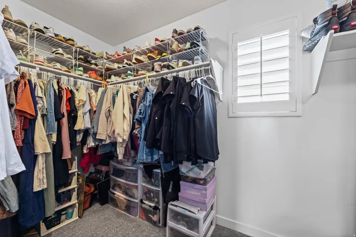 Walk-in closet featuring built-in wire shelving, hanging rods, carpet flooring, and a window with plantation shutters