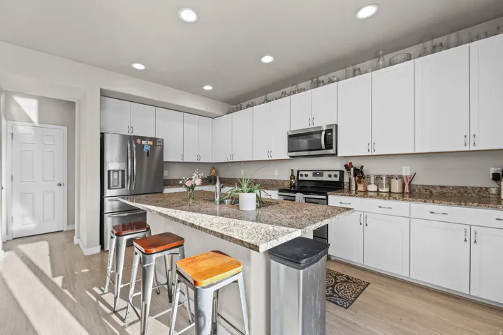 Bright kitchen featuring an expansive center island with seating, white shaker cabinetry, stainless steel appliances, and wood-finish flooring