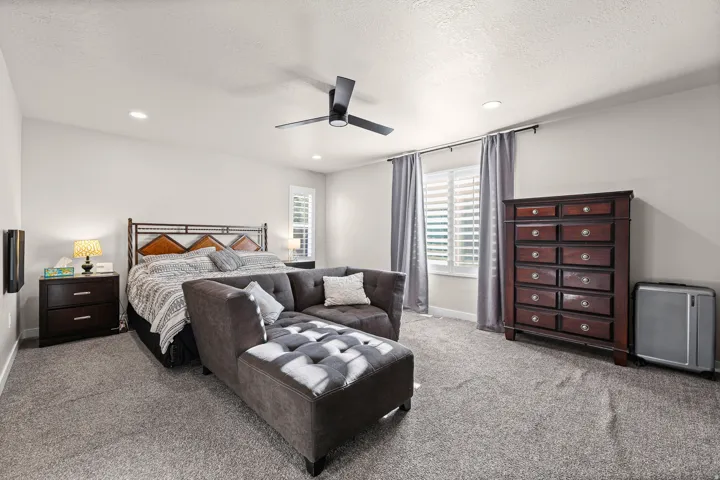 Spacious bedroom featuring neutral wall tones, recessed lighting, and a dark-toned ceiling fan