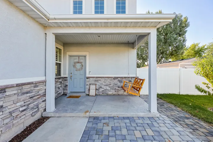 Covered porch with stone veneer accent walls, a light blue entry door, and a paver walkway