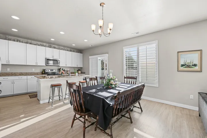 Kitchen and dining area featuring wood-finish flooring, white cabinetry, stainless steel appliances, and a kitchen island with seating