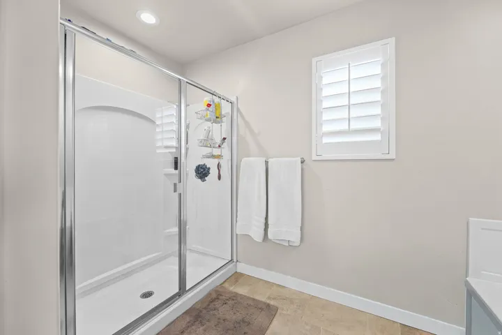 Glass-enclosed shower featuring a white surround and built-in shelving