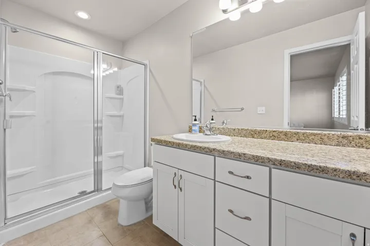 Contemporary bathroom featuring a white vanity with a light-toned countertop, a large frameless mirror, a built-in shower with clear glass enclosure, and recessed lighting