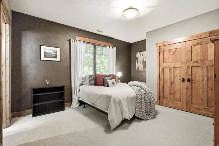 Bedroom featuring light-toned carpeting, wood-paneled closet doors, and wood trim around the window and doorways