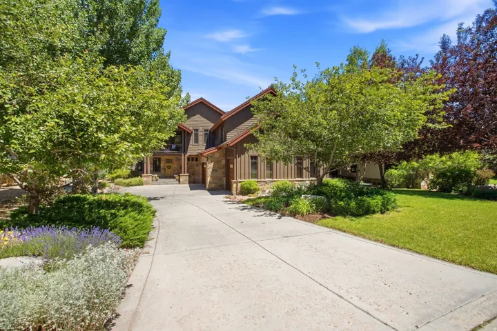 Expansive driveway leading to a multi-level residence featuring stone and wood siding, peaked rooflines, and an integrated garage