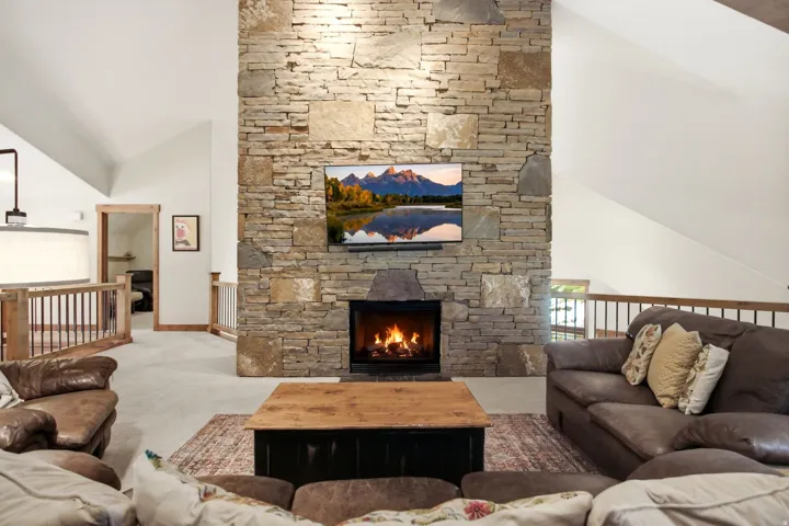 Expansive living area featuring a floor-to-ceiling stone fireplace, vaulted ceilings, and natural wood trim accents