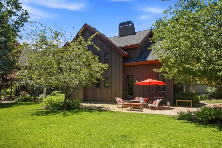 Expansive green lawn with mature trees, a brick paver patio, and dark wood-sided exterior