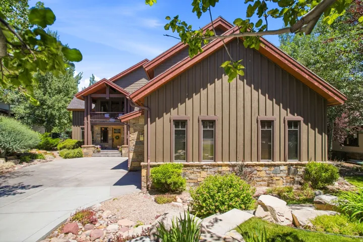 Stone and board-and-batten exterior featuring a prominent gabled roofline, a covered entrance with an upper-level balcony, and a paved driveway leading to the main entrance