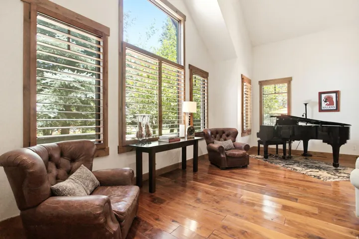 Spacious room featuring vaulted ceilings, large windows with natural wood trim, light-filtering horizontal blinds, and wood-finish flooring