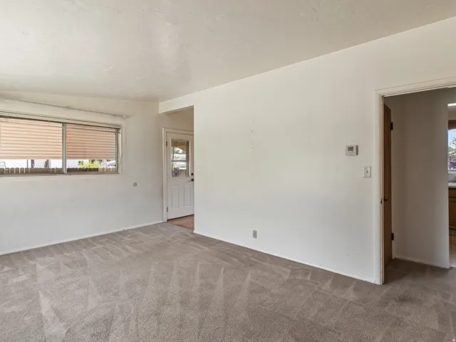 Living area featuring light-colored carpet, white walls, and a window with horizontal blinds