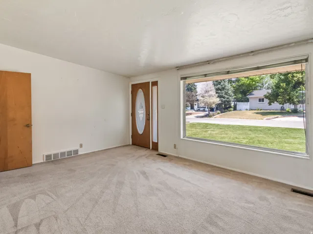 Living area featuring a large picture window, light-toned carpeting,  and a wood-panel entry door with decorative glass