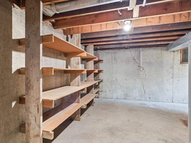 Concrete foundation walls featuring built-in wooden shelving, exposed wooden ceiling joists, and a concrete floor