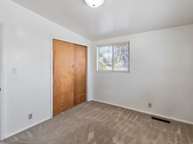 Carpeted room featuring a window with horizontal blinds, light wood-finish bi-fold closet doors, and white walls