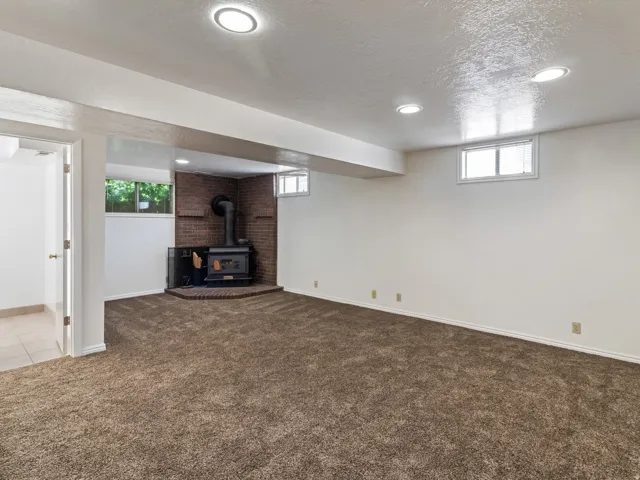 Spacious room featuring a corner wood-burning stove with a brick surround, recessed lighting, and carpeted flooring
