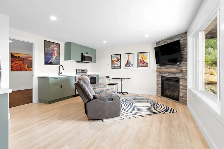 Open-concept living space featuring wood-finish flooring, a contemporary fireplace with a stone-tile surround, and a compact kitchen with green cabinetry and a white countertop