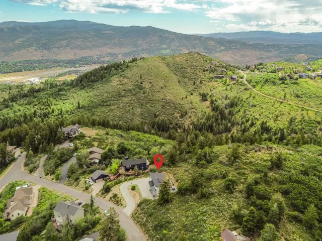 Aerial perspective showcasing a residential property nestled on a verdant hillside with winding paved roads