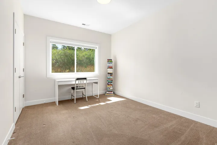 Neutral tone wall paint, light brown carpeting, and a large window with white trim