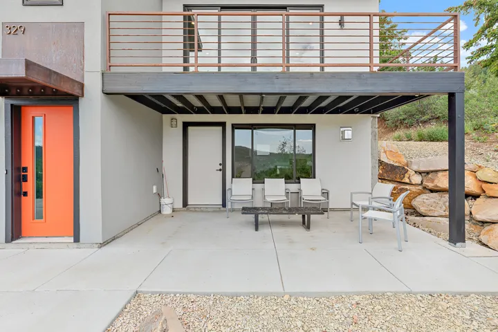 Modern exterior showcasing an orange entry door with a vertical glass insert, a steel balcony with horizontal railing, and a ground-level concrete patio