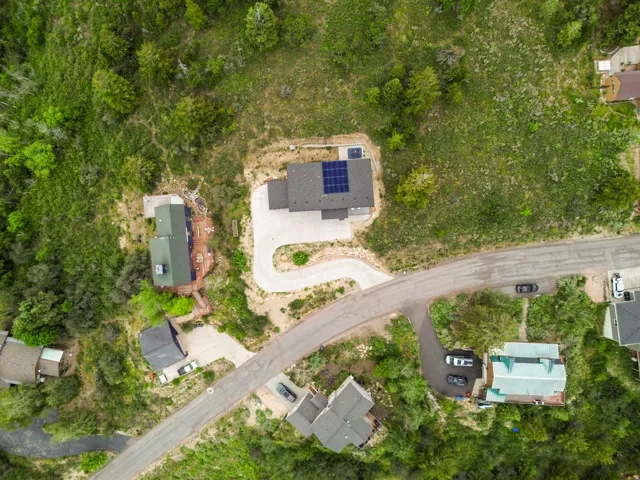 Aerial depiction of a property featuring a curved asphalt driveway, solar panels on the roof, a dark gray roofline, and surrounding natural foliage