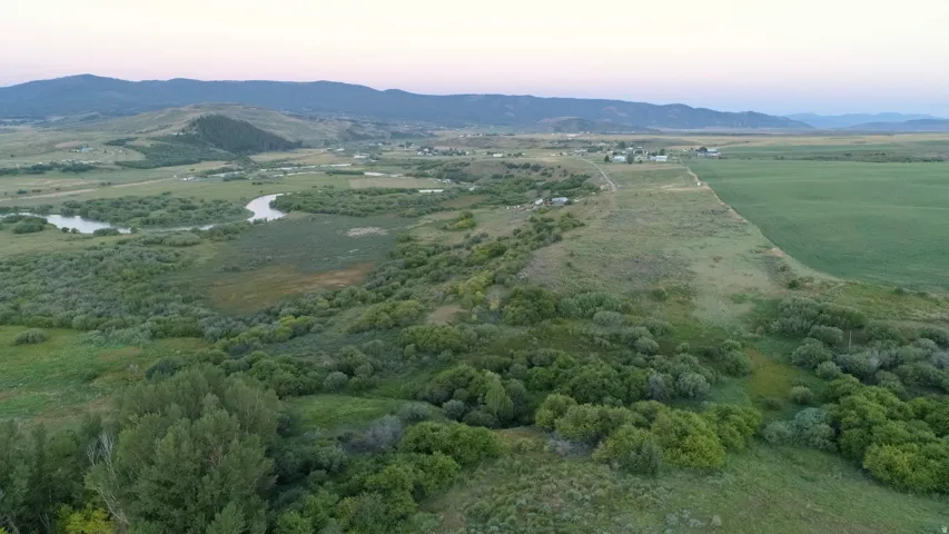 Expansive natural landscape featuring a winding river, mature trees, open fields, and distant mountains