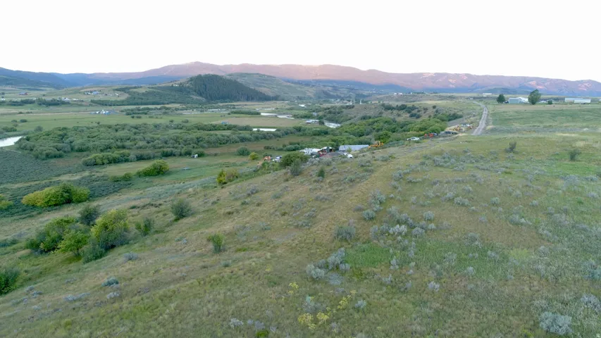Expansive rural landscape featuring rolling hills, distant mountains, a meandering river, and abundant green foliage