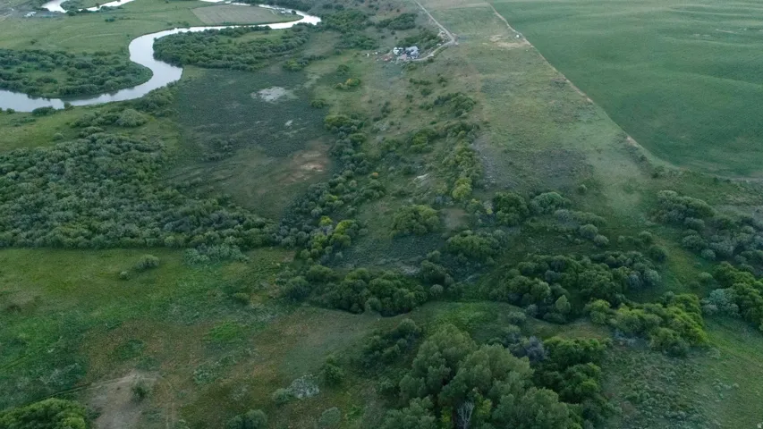Expansive landscape featuring a winding river, dense green foliage, open grassy areas, and distant agricultural fields