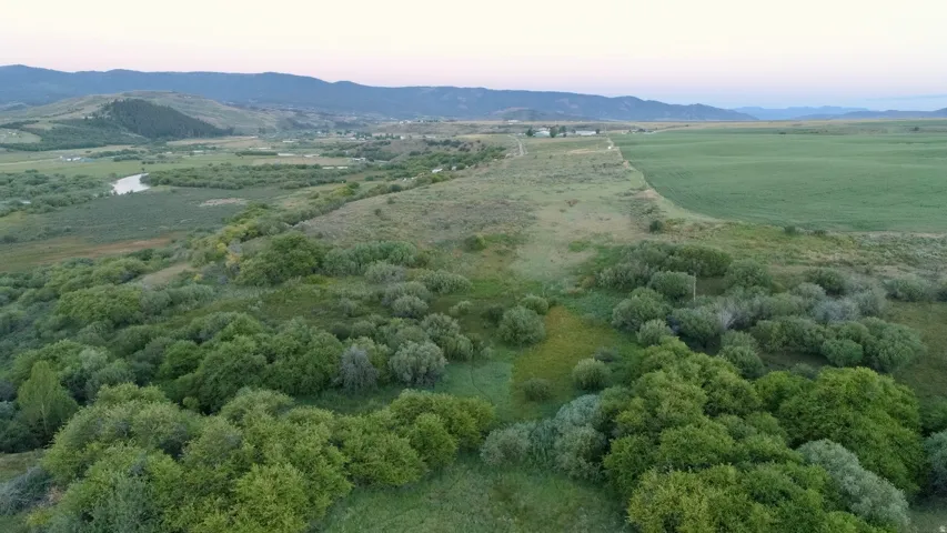 Expansive undeveloped acreage featuring diverse vegetation, a winding river, distant mountain ranges, and cultivated fields