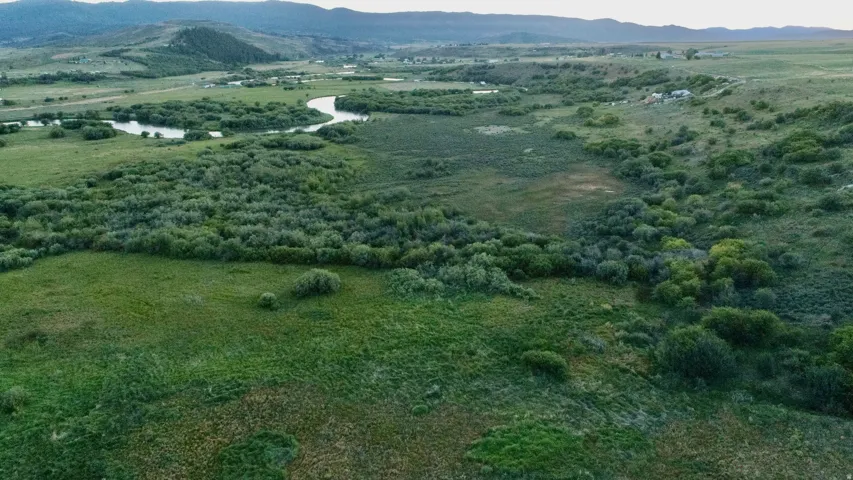 Expansive natural landscape featuring a winding river, verdant grasslands, and distant hills