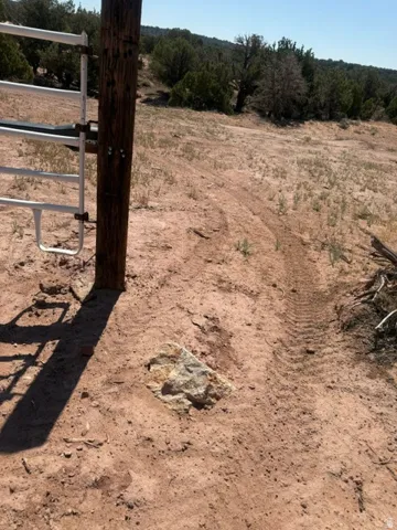 Rustic wooden fence post with a white metal gate, set against a natural landscape featuring sparse vegetation and distant trees