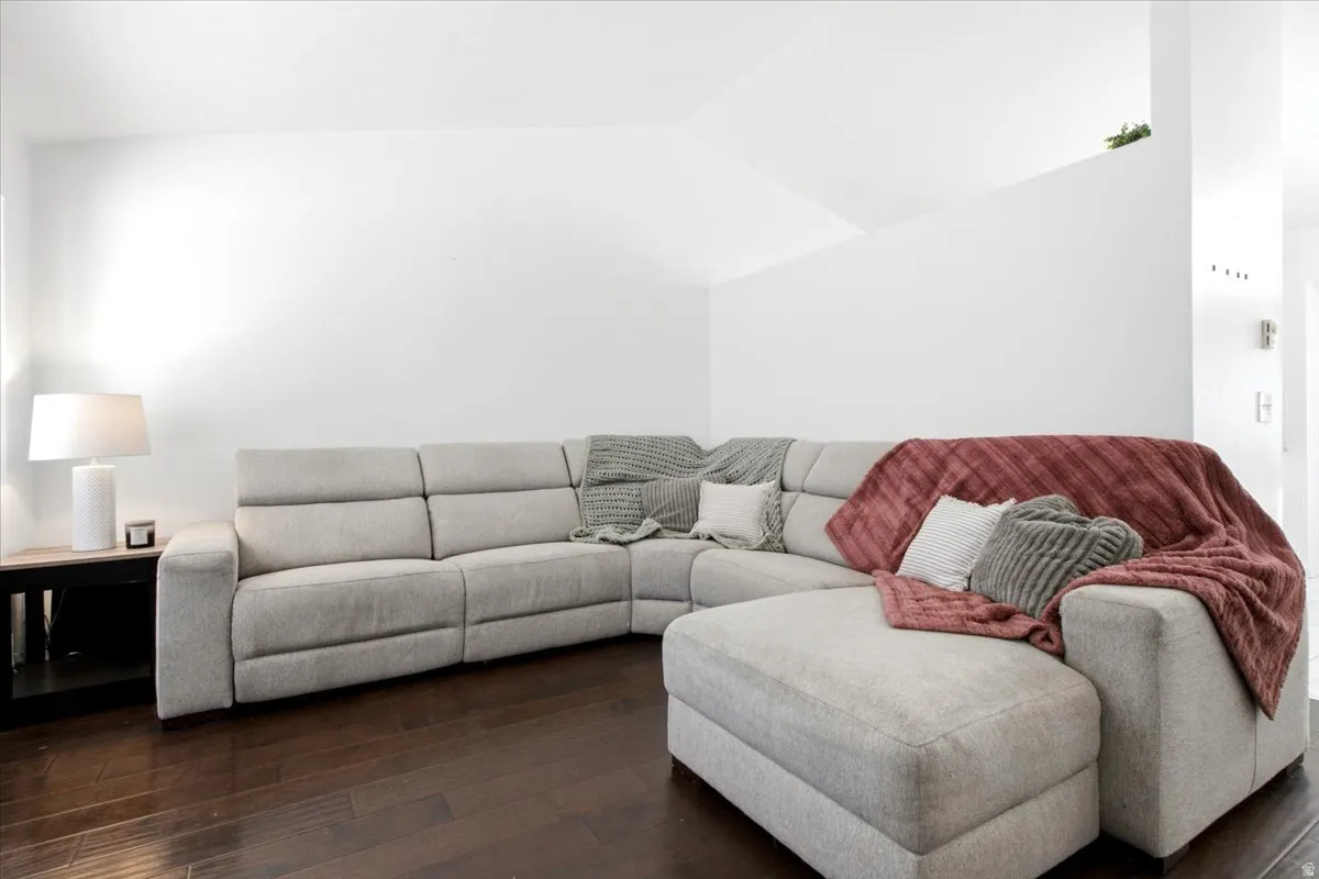 Spacious room with dark wood-finish flooring, crisp white walls, and a vaulted ceiling