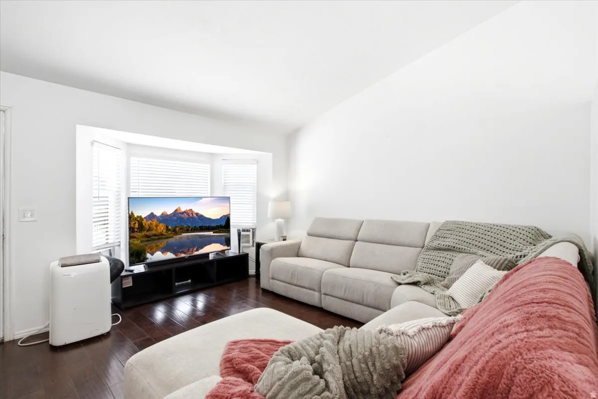 Living area featuring dark wood-finish flooring, white walls, and a bay window with blinds
