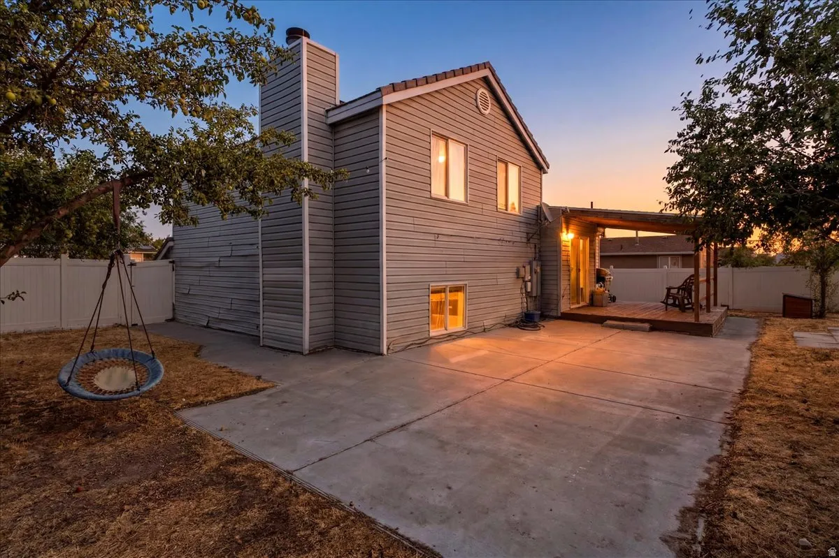 Rear exterior featuring a concrete patio, wood deck with pergola, and mature trees