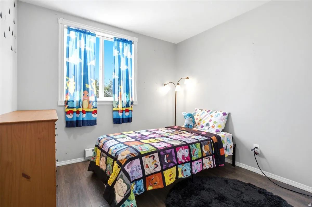 Bright bedroom featuring a large window, wood-finish flooring, light grey walls, and white trim