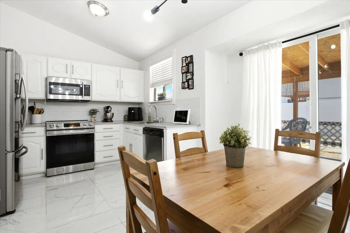 Kitchen featuring white cabinetry, stainless steel appliances, hexagon tile backsplash, and a sliding glass door leading to a covered patio