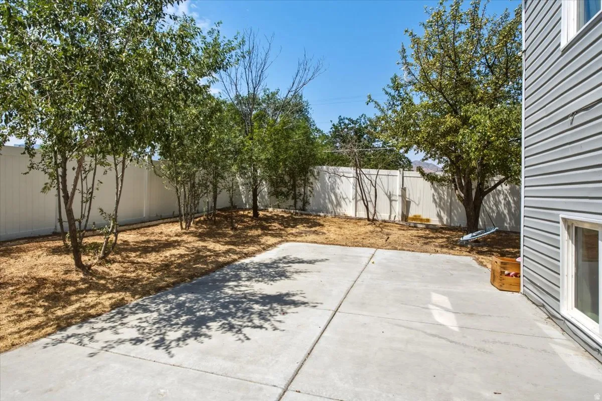 Concrete patio with a privacy fence, mature trees, and a mulched garden area