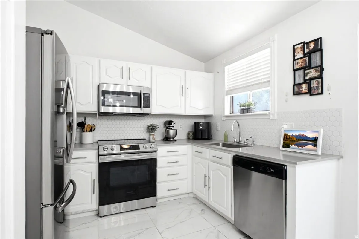 Modern kitchen featuring white cabinetry, stainless steel appliances, and a hexagon tile backsplash