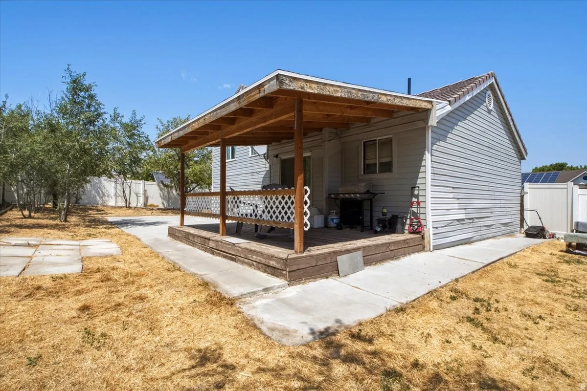 Expansive backyard featuring a covered patio, concrete walkway, and a white privacy fence