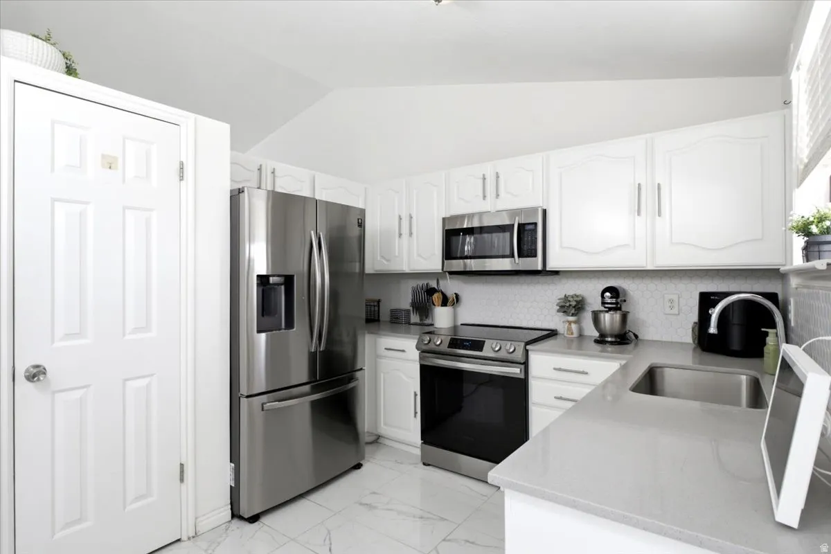 Kitchen featuring white cabinetry, stainless steel appliances, a gray countertop, a white hexagonal tile backsplash, and white tile flooring