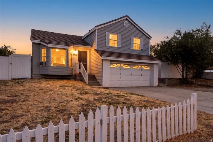 Two-story residence featuring light gray siding, a white picket fence, and a two-car garage