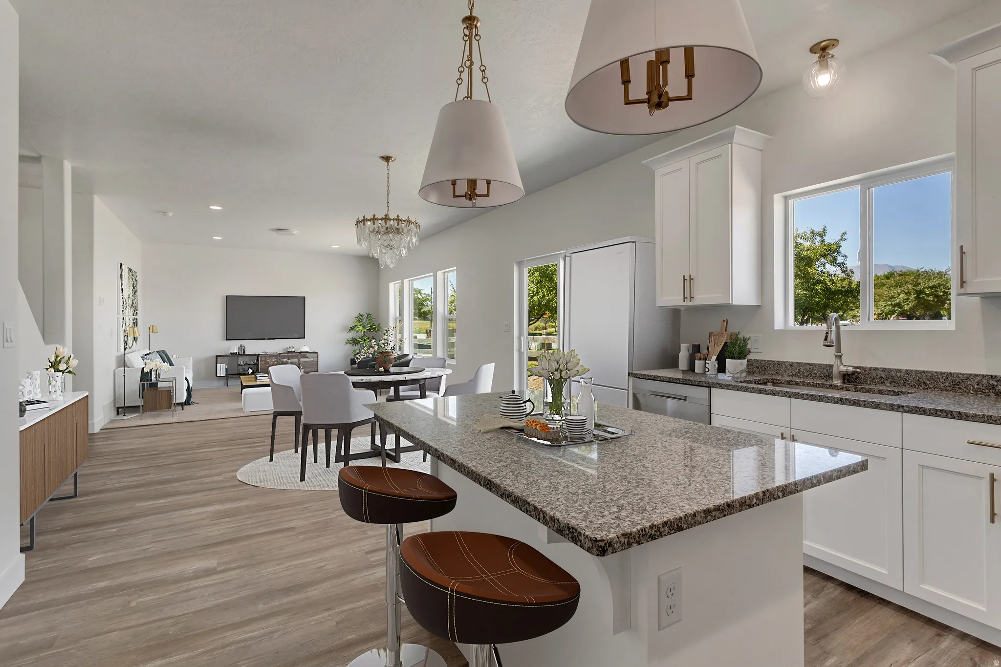 Open-concept living area featuring a kitchen island with stone-finish countertop, white cabinetry with gold-tone hardware, wood-finish flooring, and a dining area with a chandelier