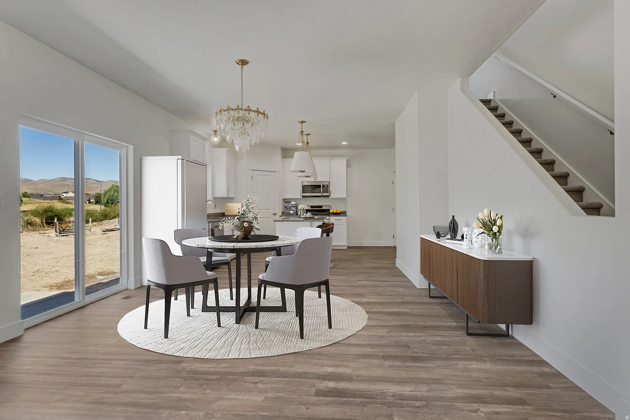 Open-concept living space featuring wood-finish flooring, a contemporary kitchen with white cabinetry, a sliding glass door to the outdoors, a staircase with carpeted treads, and a built-in wall niche