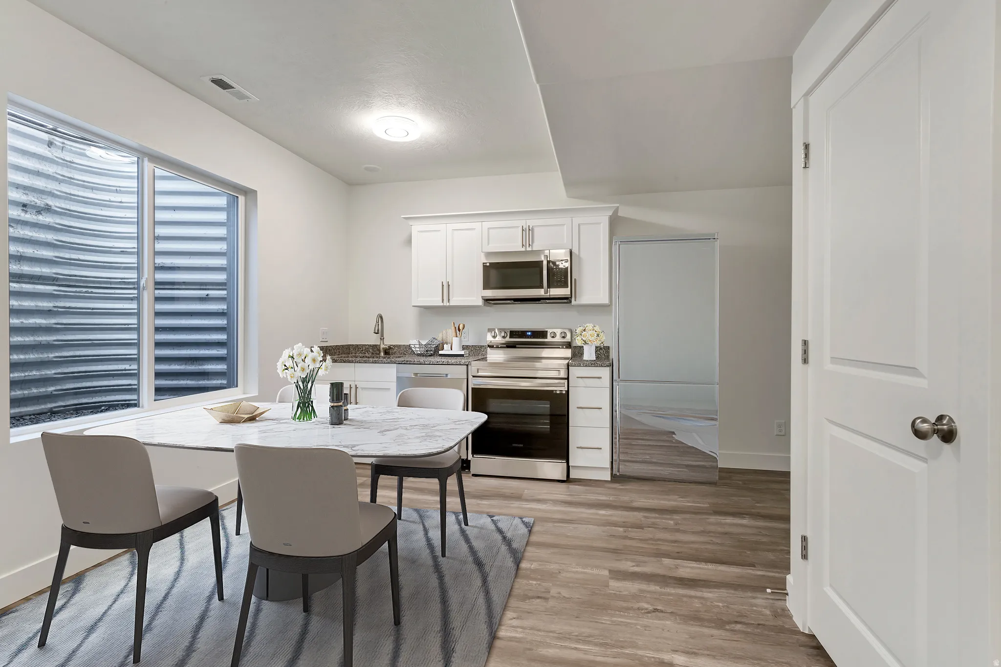 Kitchen area featuring white cabinetry, stainless steel appliances, and wood-finish flooring