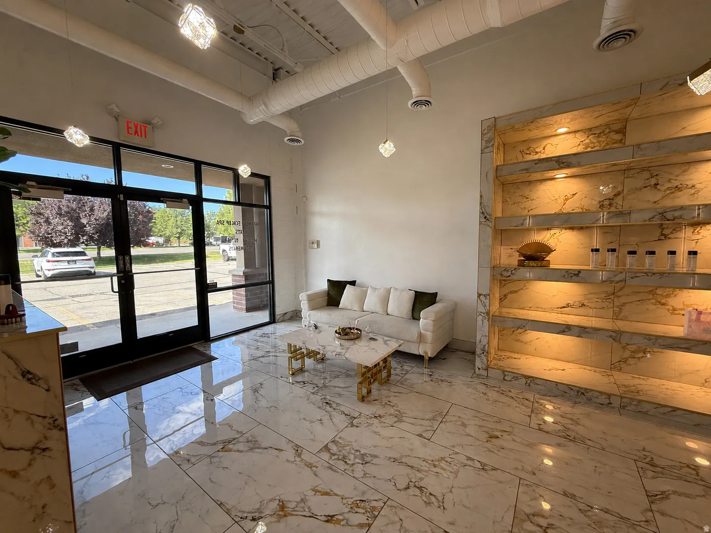Spacious entry area featuring large format white and gold veined flooring, a full glass storefront entrance, and a built-in display wall with integrated lighting