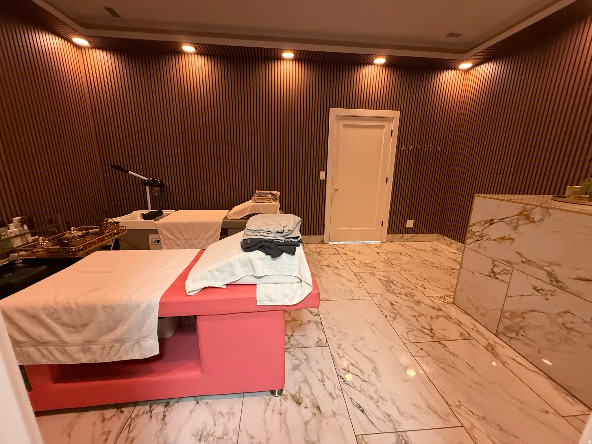 Interior space featuring vertical wood-finish wall paneling, recessed ceiling lighting, a white paneled door, and large format marble-look tile flooring